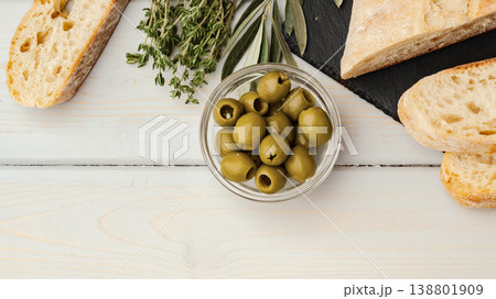 Fresh olives and bread on a wooden table with herbs in the background 138801909