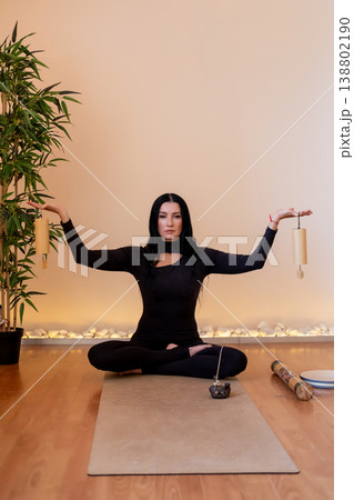 Mindfulness session. Retreat harmony. Female posing with traditional wind chime for concentration wellness session in yoga studio with bamboo plant. Mindfulness session. Retreat harmony. Female posing with traditional wind chime for concentration wellness session in yoga studio with bamboo plant. 138802190