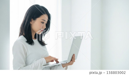 自然光あふれる白い部屋でノートPCを使う若い女性 138803002