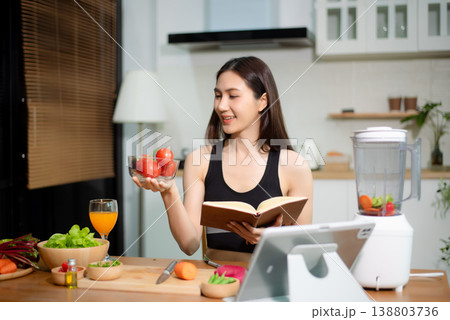 Asian woman reading recipe book while preparing fresh salad in home kitchen. Clean eating, nutrition planning, meal prep and healthy lifestyle concept. Asian woman reading recipe book while preparing fresh salad in home kitchen. Clean eating, nutrition planning, meal prep and healthy lifestyle concept. 138803736