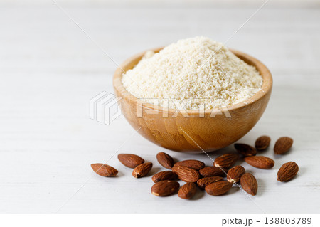 Almond meal, Almond flour, in wooden bowl with almond nuts on white table. Almond meal, Almond flour, in wooden bowl with almond nuts on white table. 138803789