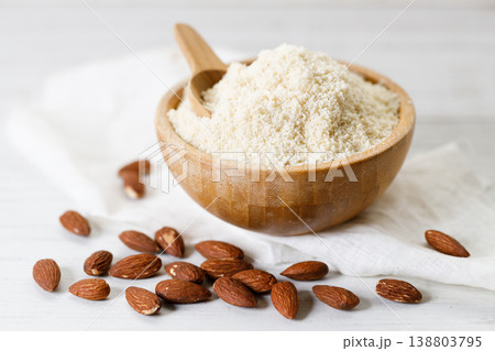 Almond meal, Almond flour, in wooden bowl with almond nuts on white table. Almond meal, Almond flour, in wooden bowl with almond nuts on white table. 138803795