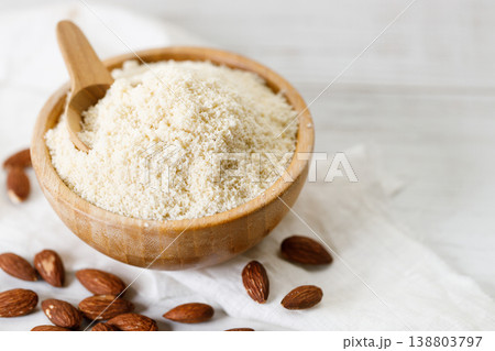 Almond meal, Almond flour, in wooden bowl with almond nuts on white table. Almond meal, Almond flour, in wooden bowl with almond nuts on white table. 138803797