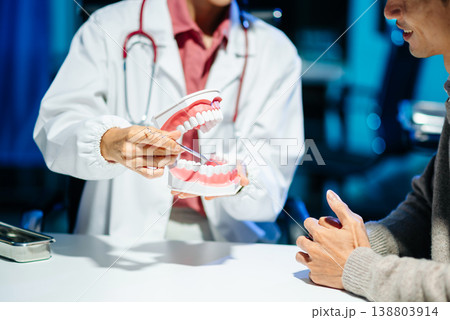 Dentist explaining tooth cleaning and oral hygiene using a dental model during consultation. Dentist explaining tooth cleaning and oral hygiene using a dental model during consultation. 138803914