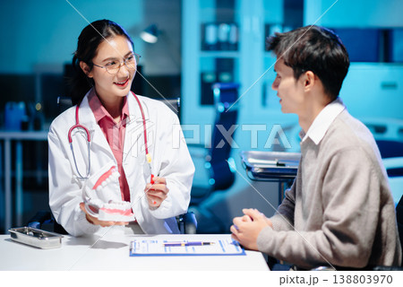 Asian female dentist holding dental model demonstrating brushing technique to young adult asian man patient Asian female dentist holding dental model demonstrating brushing technique to young adult asian man patient 138803970