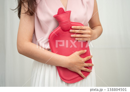 Woman using hot water bottle to relieve menstrual abdominal pain. 138804501