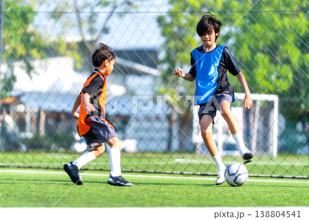 One player of blue team try to dribble the soccer ball away from the player of orange team during practice in the field with day light. 138804541