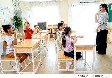 Side view of children compete to answer the question in classroom by raise their hands and wait the selection from teacher who stand in front the room. Side view of children compete to answer the question in classroom by raise their hands and wait the selection from teacher who stand in front the room. 138804585
