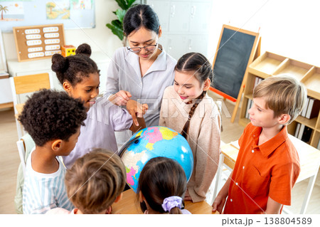 High view of teacher give the question about country on earth and tell the kids point on model globe and they look enjoy and fun with this activity. High view of teacher give the question about country on earth and tell the kids point on model globe and they look enjoy and fun with this activity. 138804589
