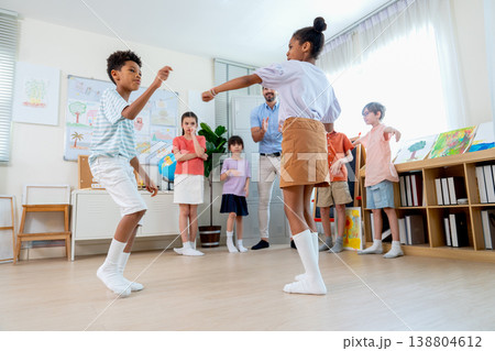 Couple of African American boy and girl enjoy to dance together and cheer up by teacher and friends in the classroom for relaxation and fun. Couple of African American boy and girl enjoy to dance together and cheer up by teacher and friends in the classroom for relaxation and fun. 138804612