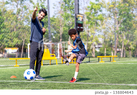 Coach point to the direction of shooting and the African American boy kick the boy to that direction during practice in the field. Coach point to the direction of shooting and the African American boy kick the boy to that direction during practice in the field. 138804643