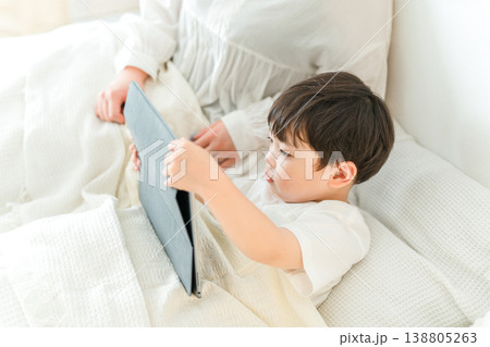 ベッドで子供にタブレットで絵本を読んであげる母親（寝かしつけ,お昼寝,読み聞かせ） 138805263