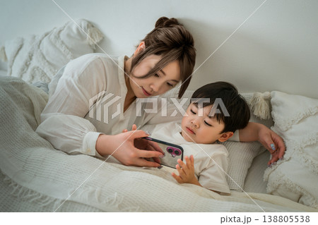 ベッドルームで男の子をスマホを使って寝かしつける母親 ベッドルームで男の子をスマホを使って寝かしつける母親 138805538