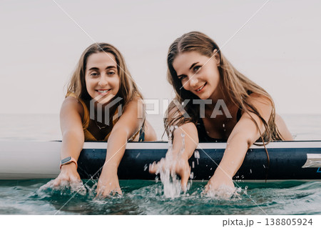 Women Paddleboard Ocean Fun - Two women are on a paddleboard, smiling, and having fun in the ocean. 138805924