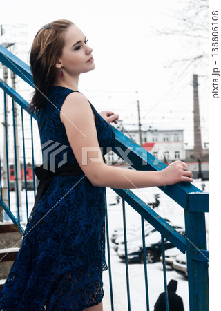 Young woman in blue dress standing on snowy bridge in winter, cold weather fashion concept 138806108