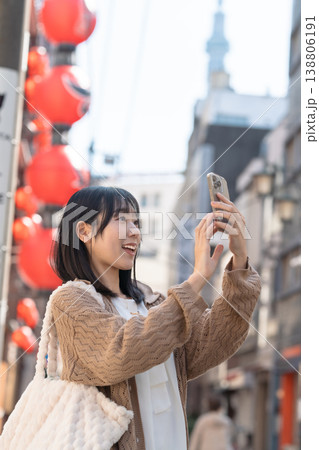 スカイツリーが見える下町を歩きながらスマホ撮影する笑顔の女性  138806191