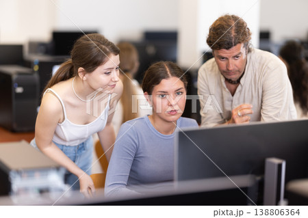 During computer lesson, two companions help girl student complete difficult task 138806364