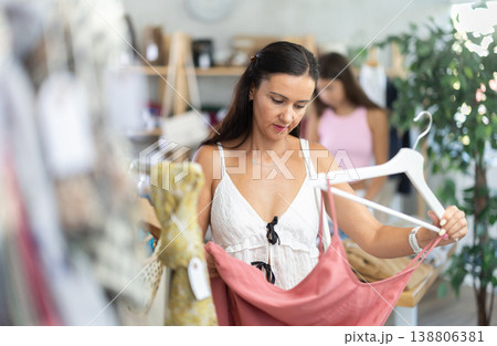 Near rack, woman buys summer dress, chooses items. Near rack, woman buys summer dress, chooses items. 138806381