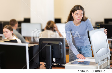 Girl puts paper document into copier, makes copy using office appliances Girl puts paper document into copier, makes copy using office appliances 138806480