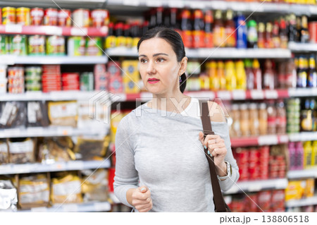 In food store, woman looking for something on shelf of showcase In food store, woman looking for something on shelf of showcase 138806518