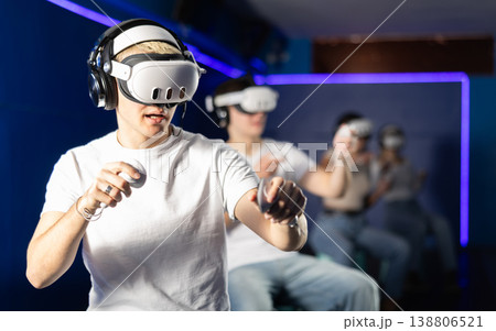 In darkened hall of gaming club, guy in VR helmet takes part in group game In darkened hall of gaming club, guy in VR helmet takes part in group game 138806521