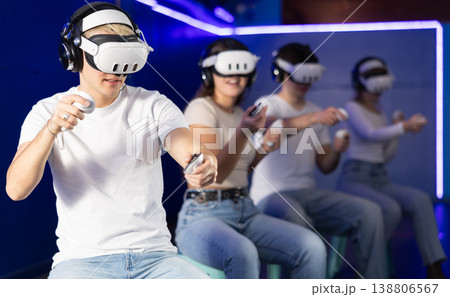 In darkened hall of gaming club, guy in VR helmet takes part in group game In darkened hall of gaming club, guy in VR helmet takes part in group game 138806567