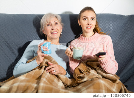 Happy elderly woman with adult daughter drinking tea and watching movie Happy elderly woman with adult daughter drinking tea and watching movie 138806740