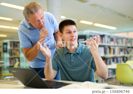 Elderly librarian asks young man who is talking loudly on mobile phone to keep quiet Elderly librarian asks young man who is talking loudly on mobile phone to keep quiet 138806746