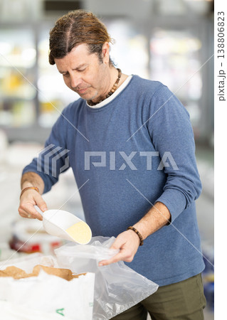 Man in store takes maize grits cereal out of sack, pours dose of cereal into bag Man in store takes maize grits cereal out of sack, pours dose of cereal into bag 138806823