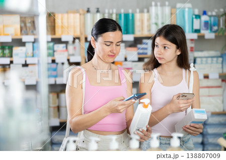 Focused family of adult woman and young girl scan QR code on label and choosing cream or skin care product in pharmacy 138807009