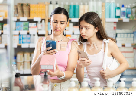 Portrait of friendly family of mother and daughter customers holding, scan QR code on label and selecting cream or skin care product in drugstore 138807017