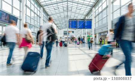 blurred motion of anonymous crowd of passengers walking with luggage inside modern bright airport terminal building near flight information departure board international journey trip 138808837