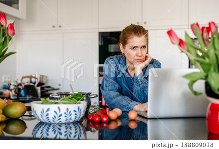 Mature woman searching recipe online on laptop while cooking in kitchen. 138809018