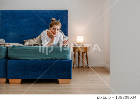 Middle aged woman using smartphone while lying in bed at home. Middle aged woman using smartphone while lying in bed at home. 138809034