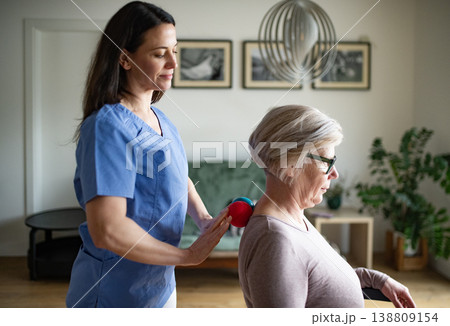 Physiotherapist helping senior woman with neck exercise, home therapy session. Physiotherapist helping senior woman with neck exercise, home therapy session. 138809154