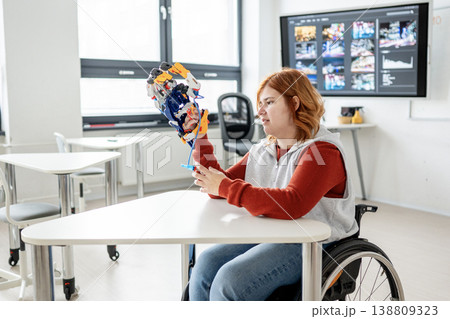 Female student in wheelchair presenting robotic project in front of classroom. Female student in wheelchair presenting robotic project in front of classroom. 138809323
