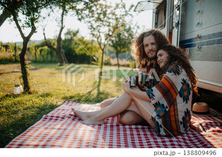Beautiful couple sitting in front of caravan under blanket, enjoying peaceful moment, drinking coffee of herbal tea. Beautiful couple sitting in front of caravan under blanket, enjoying peaceful moment, drinking coffee of herbal tea. 138809496