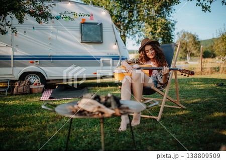 Young beautiful woman is on a camping trip in nature, sitting by tree and playing guitar. Young beautiful woman is on a camping trip in nature, sitting by tree and playing guitar. 138809509