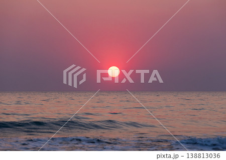 A tranquil sea view at dusk features a red pink sun sinking toward the horizon A tranquil sea view at dusk features a red pink sun sinking toward the horizon 138813036