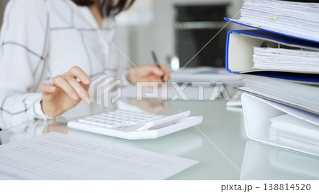 Woman working in office, calculating finances with white calculator, managing accounting paperwork and business expenses. Audit and taxes in business Woman working in office, calculating finances with white calculator, managing accounting paperwork and business expenses. Audit and taxes in business 138814520