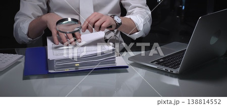 Professional examining financial documents using a magnifying glass, focusing on audit, compliance, and detailed investigation. Audit and taxes in business Professional examining financial documents using a magnifying glass, focusing on audit, compliance, and detailed investigation. Audit and taxes in business 138814552