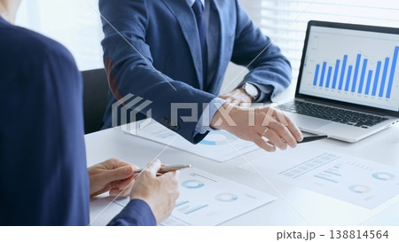 Business team analyzing financial data on a laptop and printed documents, pointing at charts and graphs during a meeting. Business people and finance concept 138814564