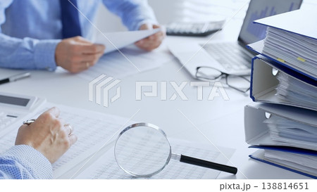 Accountants are analyzing financial reports with magnifying glass and documents, performing accounting and auditing tasks in the office, close up. Audit and taxes in business Accountants are analyzing financial reports with magnifying glass and documents, performing accounting and auditing tasks in the office, close up. Audit and taxes in business 138814651