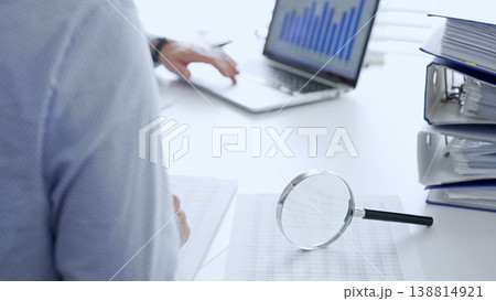 Business team working with financial data using laptop and magnifying glass, analyzing charts and checking reports, close up. Audit and taxes in business 138814921