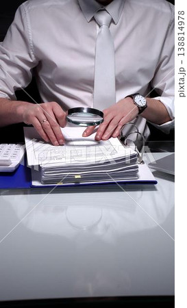Professional businessman analyzing financial reports and charts with a magnifying glass while working at a desk. Audit and taxes theme in business Professional businessman analyzing financial reports and charts with a magnifying glass while working at a desk. Audit and taxes theme in business 138814978