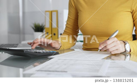 Woman calculating budget and reviewing financial documents using a laptop and calculator for home finances. Audit and taxes in business Woman calculating budget and reviewing financial documents using a laptop and calculator for home finances. Audit and taxes in business 138815201