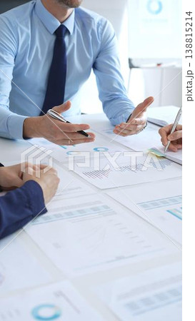 Group of business people professionals discussing financial reports with graphs and charts on a desk during a corporate meeting, highlighting teamwork, planning, and strategy Group of business people professionals discussing financial reports with graphs and charts on a desk during a corporate meeting, highlighting teamwork, planning, and strategy 138815214