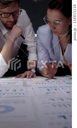 Business professionals collaborating on a strategic project. Analyzing financial data and charts on a laptop and documents. Working late in a dark modern office 138815216