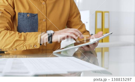 Person using a digital tablet for business at desk, navigating online content or browsing documents. Audit and taxes in business Person using a digital tablet for business at desk, navigating online content or browsing documents. Audit and taxes in business 138815297