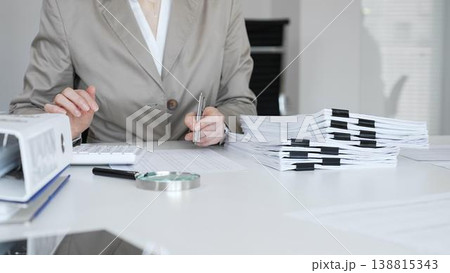 Businesswoman reviewing financial reports, calculating taxes, and managing audit paperwork in a busy office setting. Audit and taxes concept Businesswoman reviewing financial reports, calculating taxes, and managing audit paperwork in a busy office setting. Audit and taxes concept 138815343